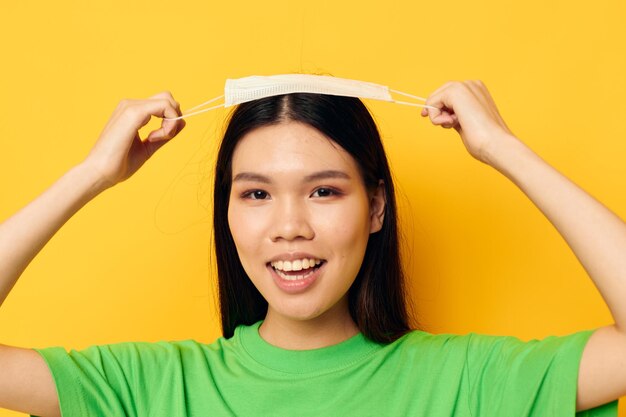 Encantadora joven asiática con una máscara médica en la protección de la mano con fondo amarillo inalterado