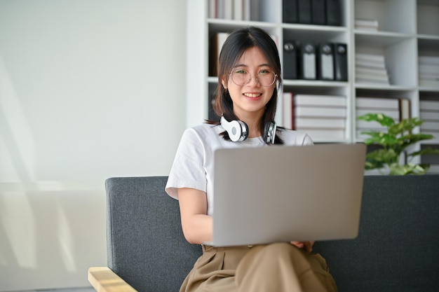 Una encantadora joven asiática usando su computadora portátil en un sofá en su sala de estar