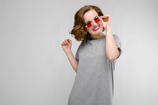 Encantadora joven en una camiseta gris un gris. Chica con gafas rojas de ojos cuadrados.