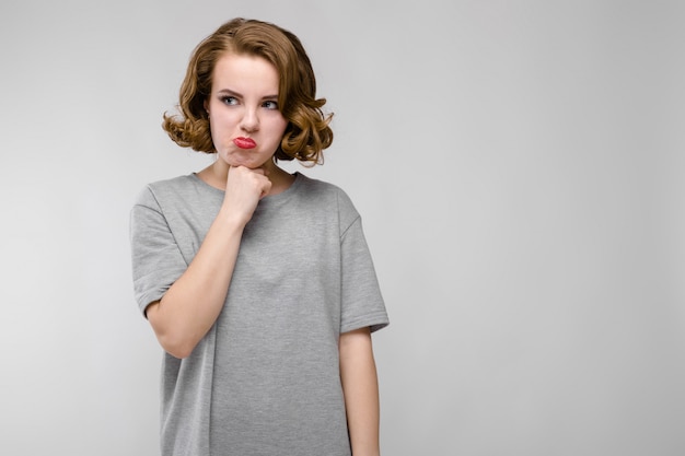 Encantadora joven en una camiseta gris sobre un fondo gris. La niña se inmovilizó la barbilla.