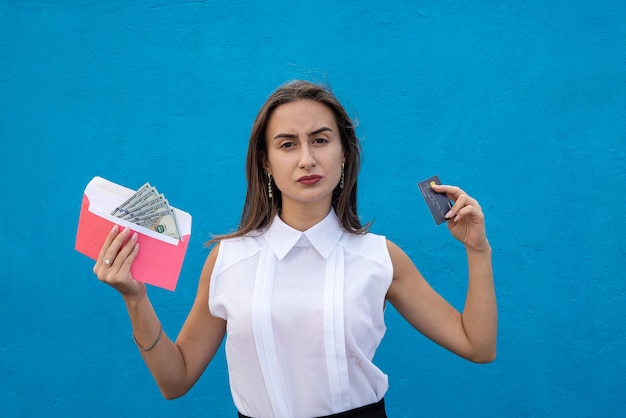 Encantadora joven empresaria sosteniendo dólares en un sobre y una tarjeta de crédito para ir de compras