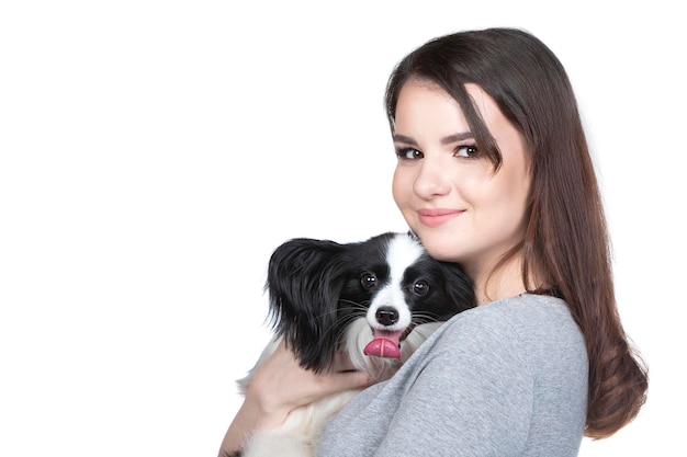 Una encantadora joven está abrazando a su cachorro papillon y mirando la cummera