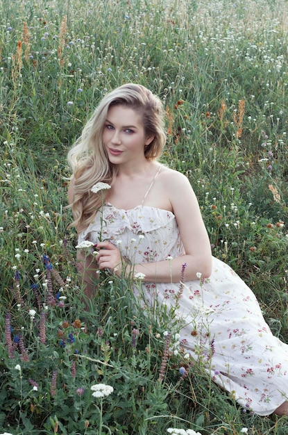 Encantadora joven hermosa mujer rubia usa un vestido blanco de verano con estampado floral en flores de campo