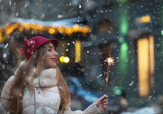 Encantadora joven jugando con bengalas en la calle durante las nevadas. Espacio vacio