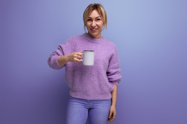 Encantadora joven milenaria rubia con un look casual se vigoriza con una taza de café en un brillante