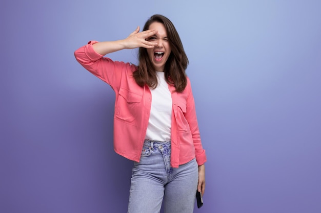 Encantadora joven morena sonriente con una camisa rosa y jeans en un estudio de fondo aislado