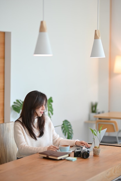 Encantadora joven mujer asiática café o blogger de viajes trabajando en su computadora portátil en la cafetería moderna