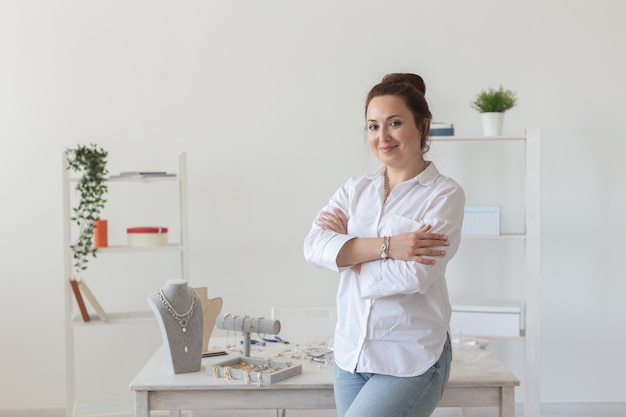 Encantadora joven mujer caucásica entusiasta haciendo hermosas joyas de fantasía únicas mientras está sentada en su escritorio. Concepto de afición y trabajo agradable.