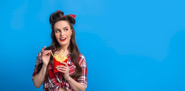 Encantadora joven mujer pinup en ropa retro comiendo papas fritas del paquete mirando el espacio de la copia