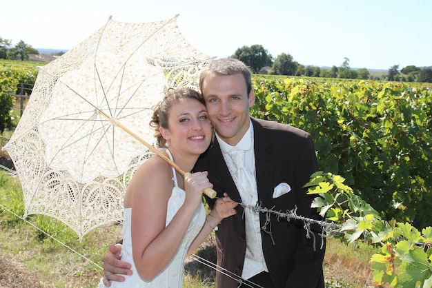 encantadora joven pareja de novios en viñedos en verano con paraguas blanco
