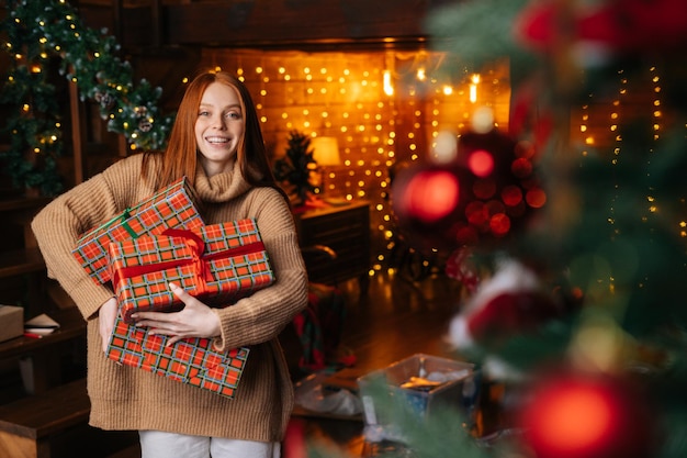 Encantadora joven pelirroja sonriente sosteniendo muchas hermosas cajas de regalo de Navidad