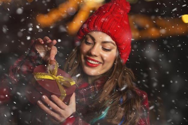 Encantadora joven recibiendo un regalo en el mercado de Navidad durante las nevadas. Espacio para texto