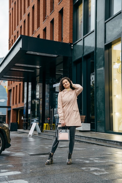 Encantadora joven rizada con hermosa sonrisa caminando por la calle de la ciudad en día lluvioso