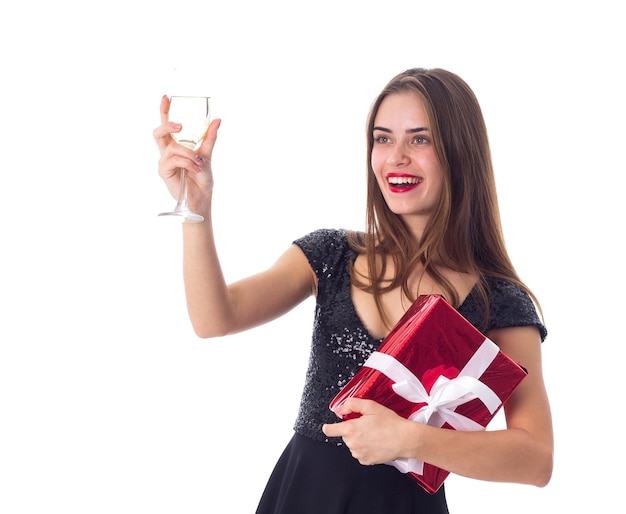 Encantadora joven vestida de negro sosteniendo un regalo rojo con cinta blanca y una copa de champán