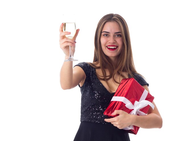 Encantadora joven vestida de negro sosteniendo un regalo rojo con cinta blanca y una copa de champán