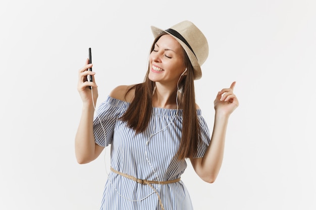 Encantadora joven vestida, sombrero escuchando música en auriculares en el teléfono móvil, disfrutar, relajarse aislado sobre fondo blanco. Gente, emociones sinceras, concepto de estilo de vida. Área de publicidad. Copie el espacio.