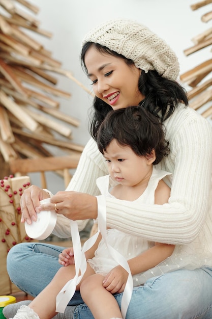 Encantadora madre e hija desenrollando la cinta blanca para la decoración de regalos de navidad
