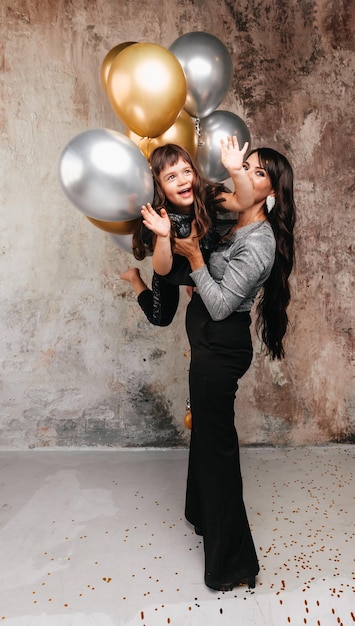Encantadora madre e hija con el mismo atuendo posan juntas después de una fiesta de cumpleaños Retrato de una encantadora niña abrazando a su hija con globos
