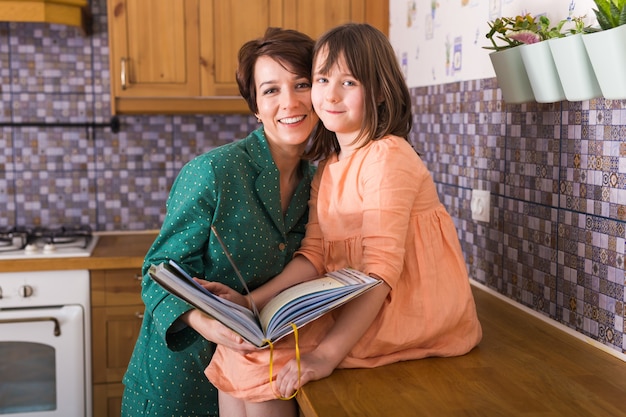 Encantadora madre está mostrando imágenes en un libro a su linda hijita en casa