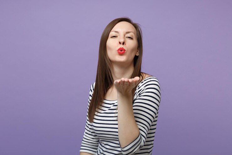 Foto encantadora menina morena jovem bonita em roupas listradas casuais posando isolado no retrato de estúdio de fundo roxo violeta. conceito de estilo de vida de pessoas. mock up espaço de cópia. soprando mandando beijo no ar.