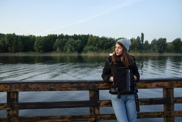 Encantadora morena de pie en el muelle de madera y mirando a un lado