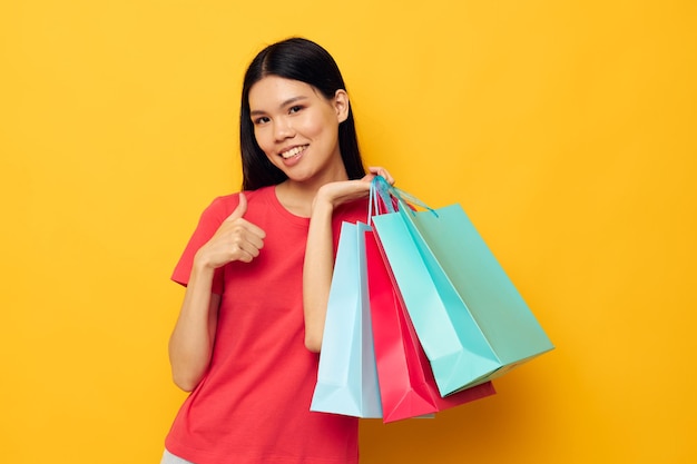 Encantadora mujer asiática joven con bolsas de colores posando compras divertido fondo amarillo inalterado