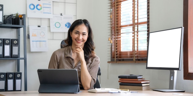 Encantadora mujer asiática trabajando en la oficina usando una laptop Mirando la cámara