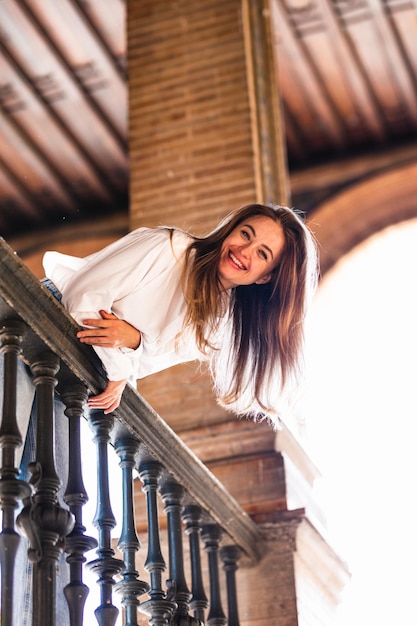 Encantadora mujer caucásica sonriente apoyada en la baranda de un balcón en la Plaza de España en Sevilla