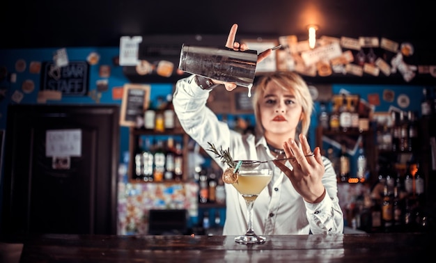 Encantadora mujer coctelería demuestra sus habilidades en el mostrador mientras está de pie cerca del mostrador del bar en la discoteca