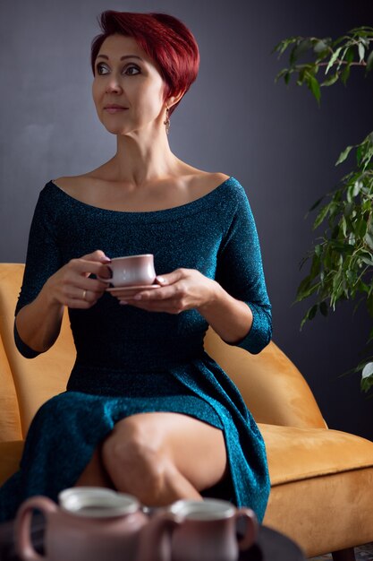 Encantadora mujer en elegante vestido de noche y peinado brillante con una taza de café caliente