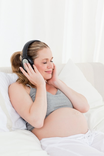 Encantadora mujer embarazada escuchando música en su cama