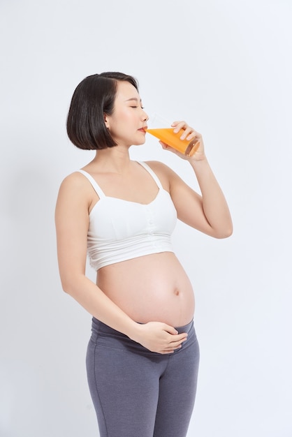 Encantadora mujer embarazada sosteniendo un vaso de jugo de naranja mientras está de pie