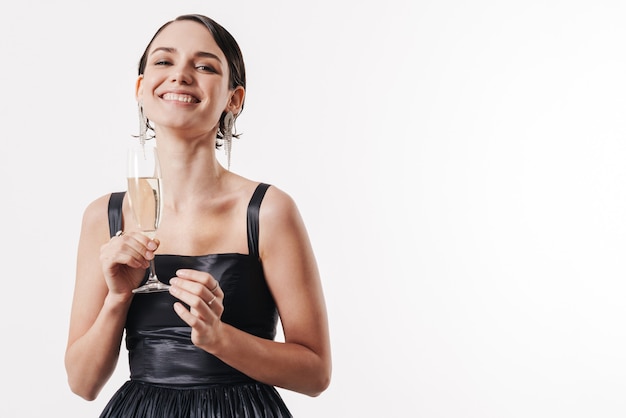 Encantadora mujer feliz glamorosa joven sonriendo y sosteniendo una copa de champán aislado sobre la pared blanca