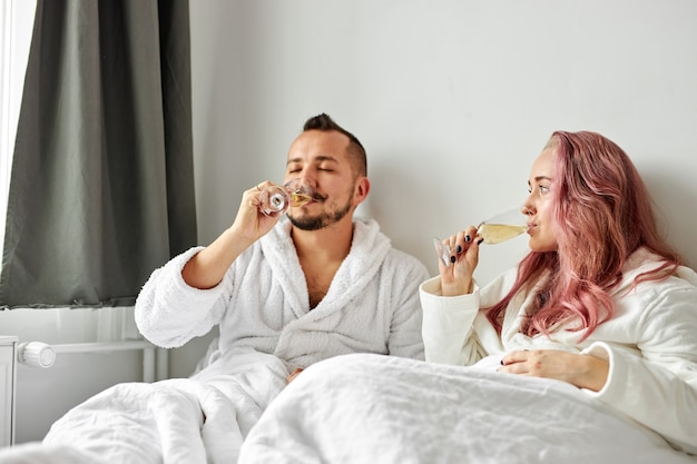 Encantadora mujer y hombre en túnicas blancas acostado en la cama y disfrutando de tiempo juntos