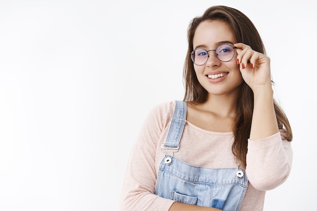 Encantadora mujer inteligente asertiva en monos sosteniendo gafas en la mano y sonriendo ampliamente