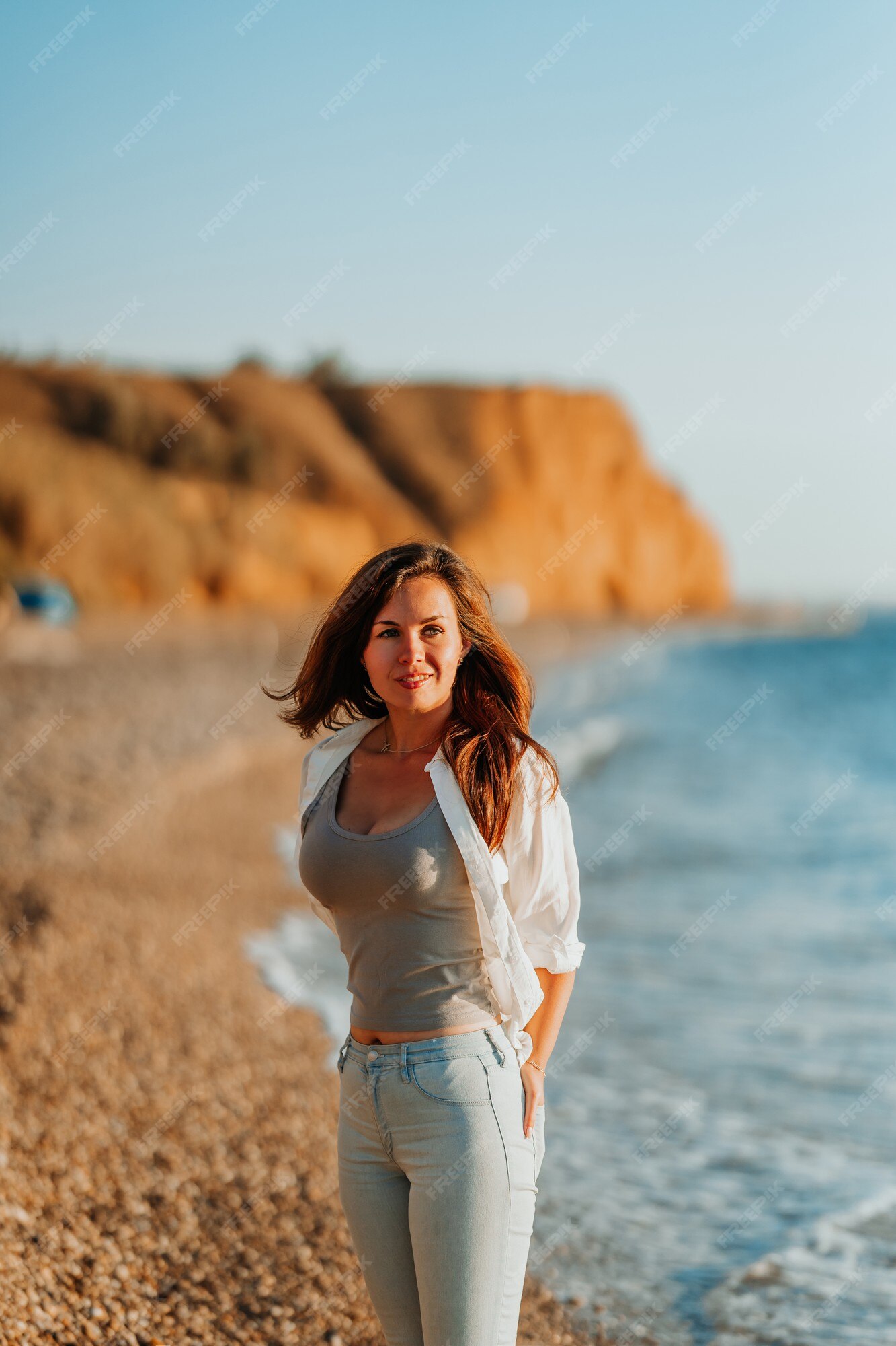Una encantadora joven con camisa blanca y jeans en una playa romántica junto al mar | Foto