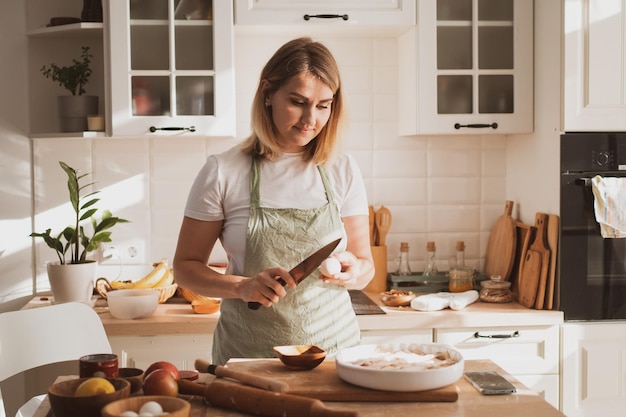 Encantadora mujer joven en delantal de chef preparando pastel en casa en la cocina Acogedor interior de casa