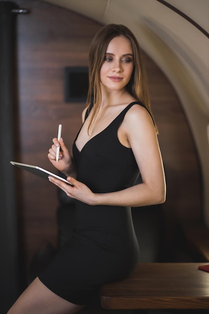 Encantadora mujer joven esbelta con sexy vestido negro en jet privado. Empresario joven exitoso sosteniendo tableta digital, trabajando durante el vuelo. Concepto de tecnología.