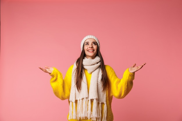 Encantadora mujer joven con gorro y bufanda que se encuentran aisladas sobre rosa, posando