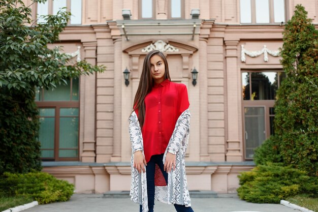 Encantadora mujer joven con un magnífico cabello moreno, ojos grandes, un hermoso lápiz labial rojo y una apariencia elegante. Una joven atractiva corre por el centro de la ciudad, se vuelve hacia la cámara y sonríe.