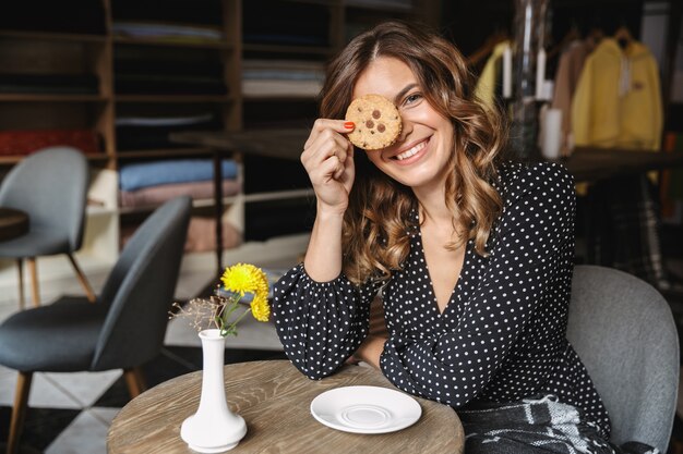 Encantadora mujer joven sentada en el café en el interior, comiendo cookis