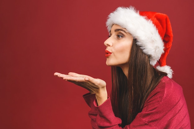 Encantadora mujer joven en suéter de Navidad y gorro de Papá Noel, envía un beso