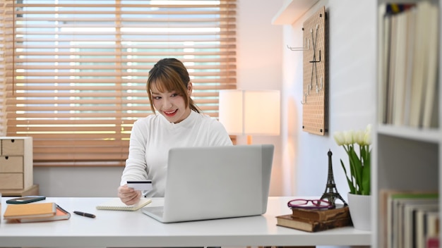 Encantadora mujer joven con tarjeta de crédito y usando una computadora portátil comprando productos a través de compras en línea