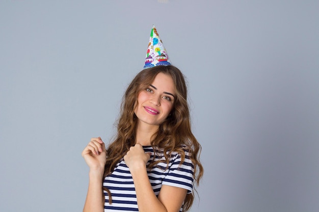 Encantadora mujer joven vestida con camiseta despojada y gorra de celebración sobre fondo gris en el estudio