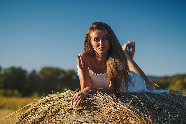 Encantadora mujer joven en vestido blanco junto al pajar. Retrato femenino en campo en campo.