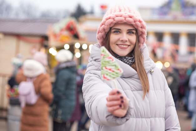 Encantadora mujer joven viste sombrero rosa y abrigo gris con caramelos en la calle Feria de Navidad. Espacio para texto