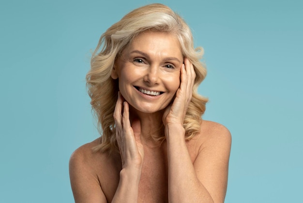 Encantadora mujer madura de los años 50 cogida de la mano en la cara sonriendo a la cámara aislada de fondo azul