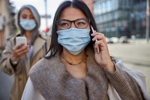 Encantadora mujer en máscara médica con conversación telefónica al aire libre