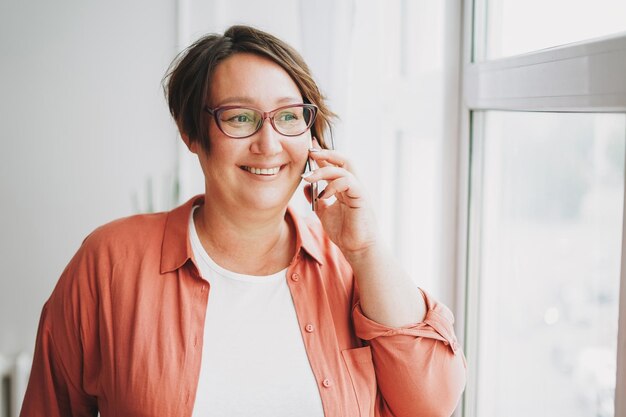 Encantadora mujer morena adulta empresaria con gafas de talla grande cuerpo positivo usando el móvil