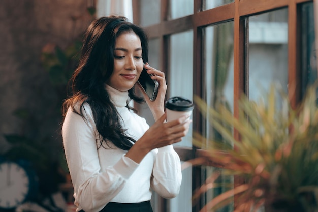 Encantadora mujer de negocios asiática inteligente que usa una computadora portátil para trabajar en la empresa de capacitación seminario de desarrollo profesional sentarse en la mesa sostener una taza de comida para llevar bebida caliente en la oficina del loft o en la cafetería estilo de vida de trabajo independiente